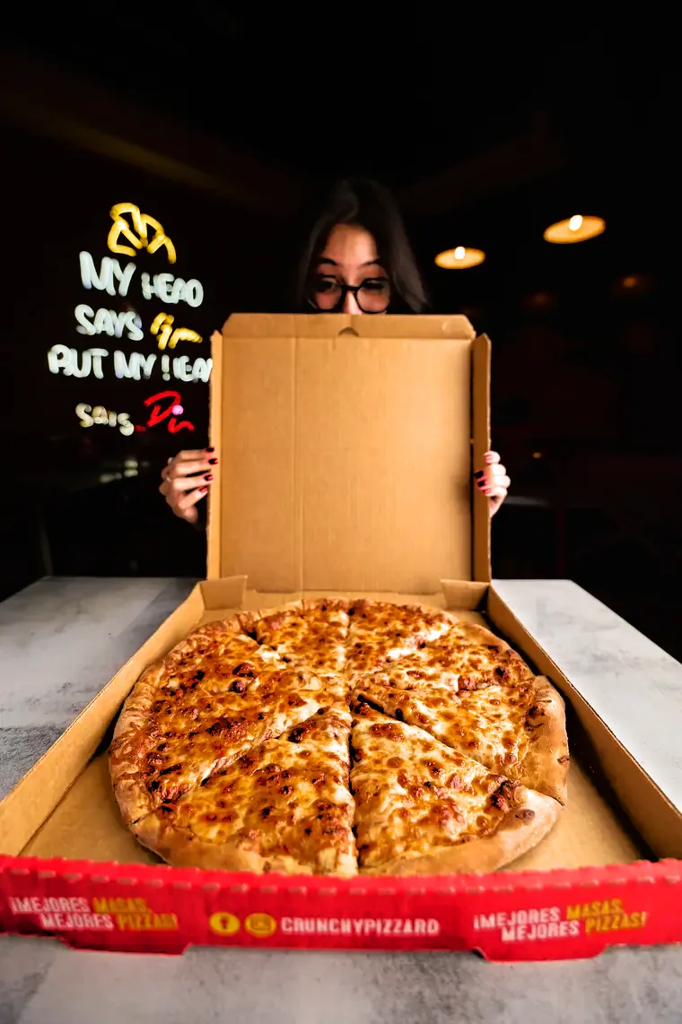 Pizza de Crunchy Pizza en su caja, con el letrero de la tienda al fondo